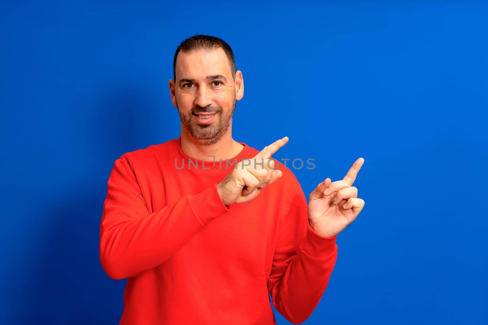 Hispanic man with beard pointing index fingers to the side in copy space mock up isolated on blue colored background studio portrait