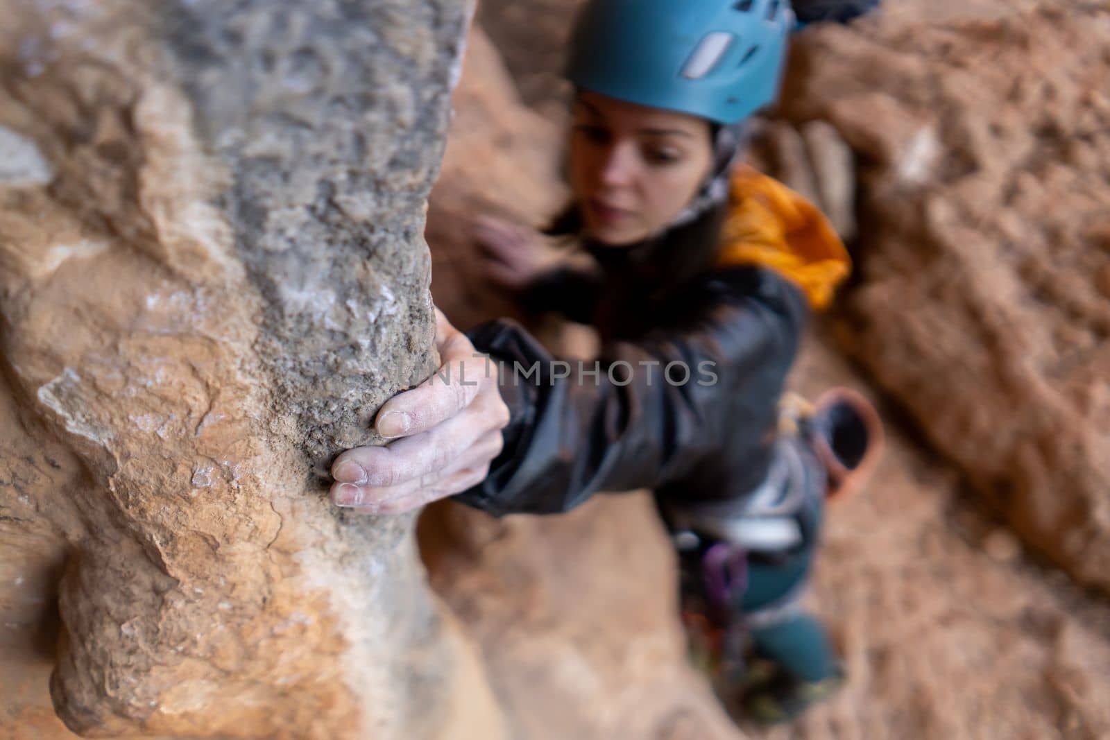 Young girl is engaged in extreme sports, fearlessly climbs up the rock using white magnesia powder, holds her hand to the ledge in the relief, close-up view, focus on the finger, the girl is blurred.