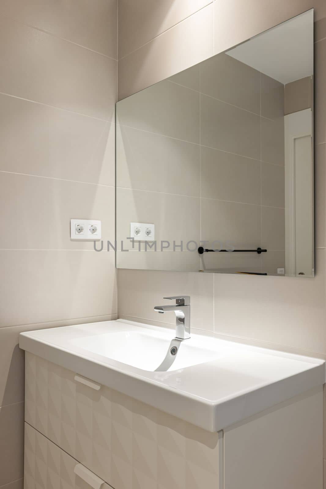 Simple, empty and modern bathroom with beige tiles, sink and mirror.