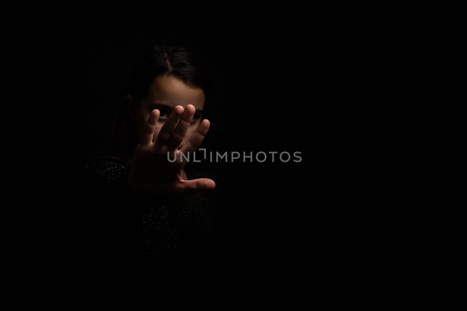 little girl with a raised hand making a stop sign gesture on a black background. Violence, harassment and child abuse prevention concept