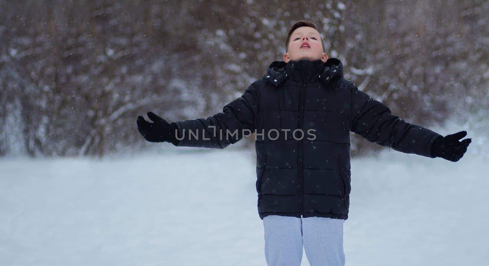 A boy in winter clothes raises his hands up against the background of winter nature. by gelog67