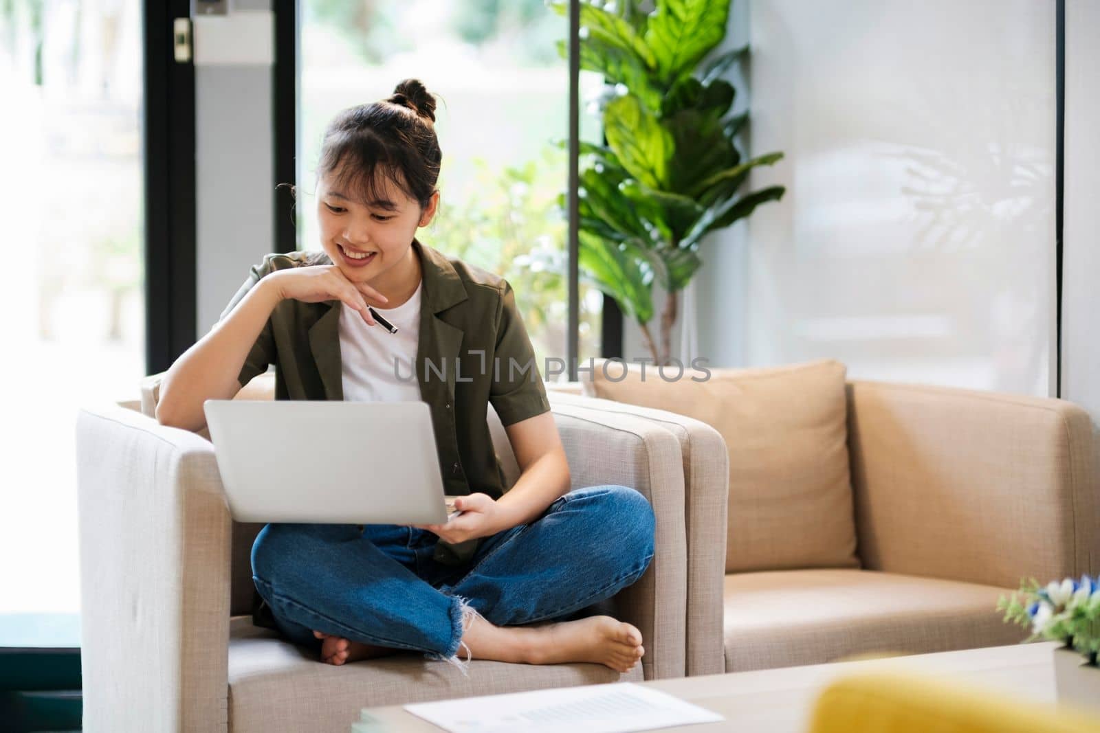 Young asian woman studying, online leading, and listening to music with headset while sitting on couch at home. Listening to podcast, audio book, watching videos using laptop.