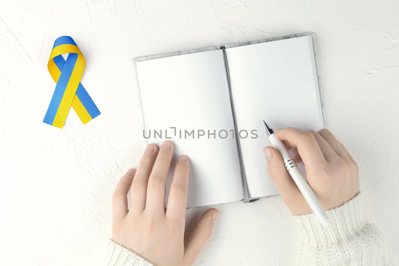 female hands with pen an open blank notepad and yellow blue ribbon on white table. concept needs help and support, truth will win