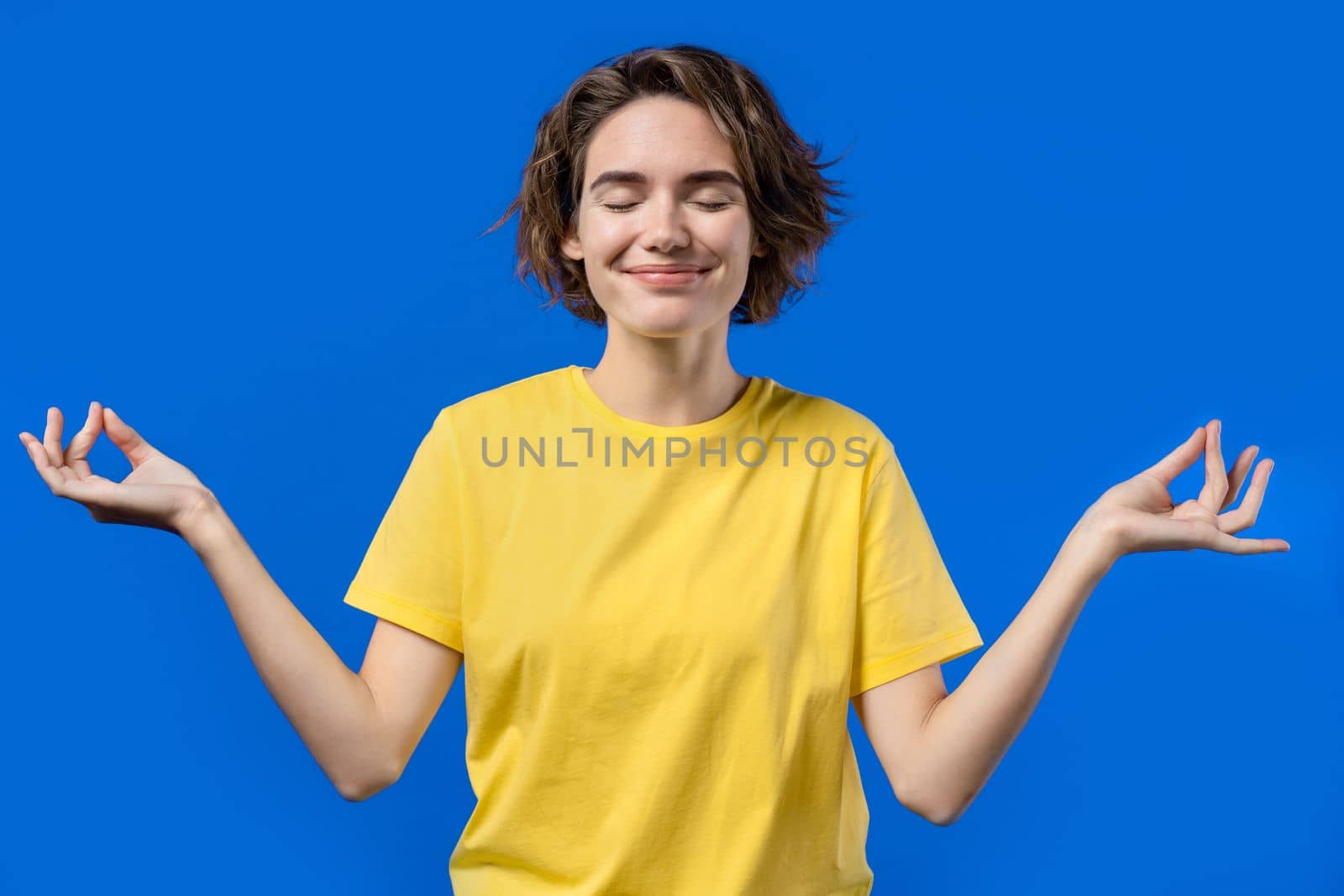 Calm woman relaxing, meditating, refuses stress. Sunny girl breathes deeply, calms down blue studio background. Yoga, moral balance, zen concept. High quality photo