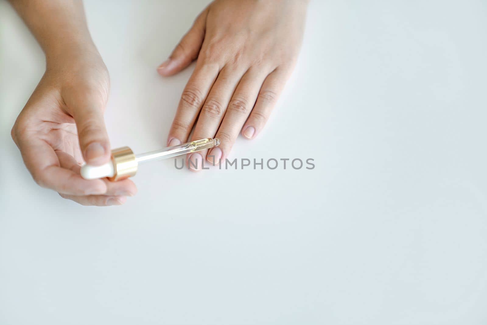 Nail and hand skin care. Woman holds pipette with oil to apply to her nails for treatment and strengthening of nails. Hands close-up, copy space by Laguna781