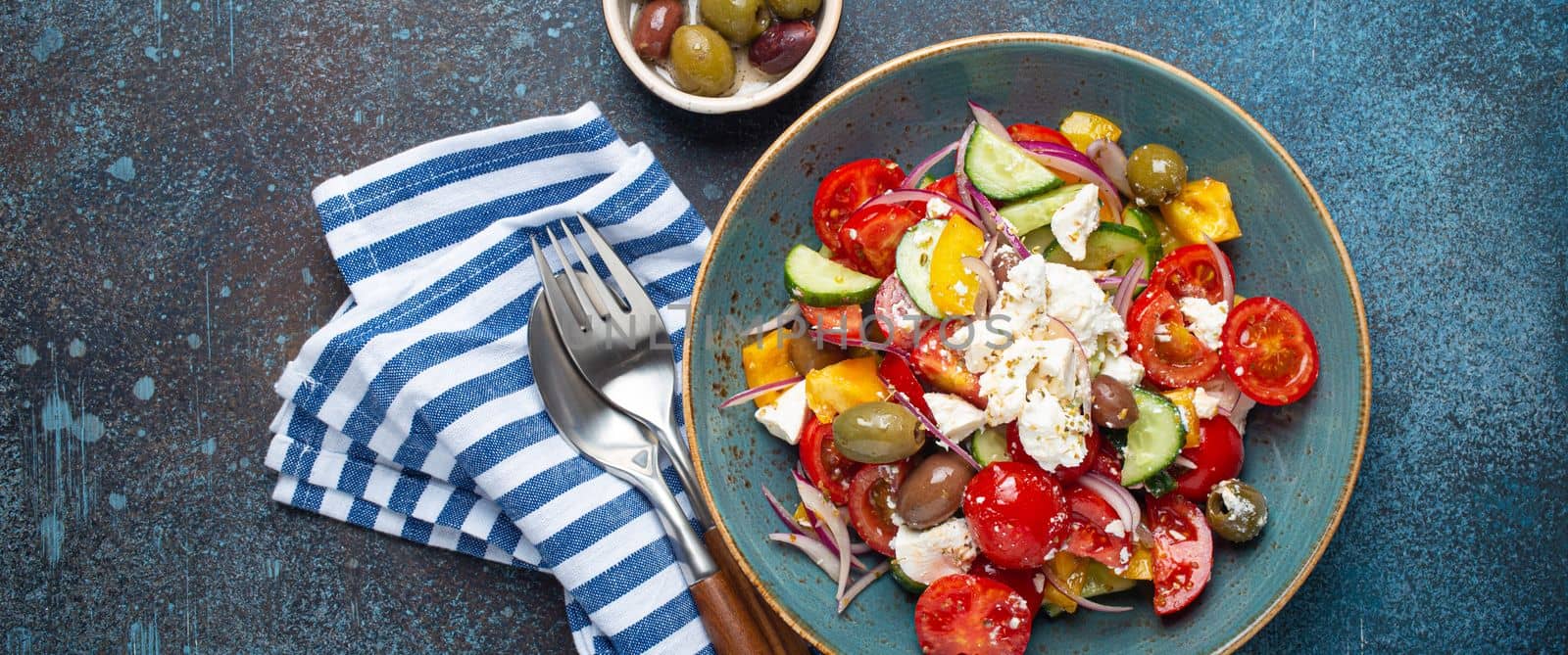 Greek salad with feta cheese, vegetables, olives in blue bowl on concrete background by its_al_dente