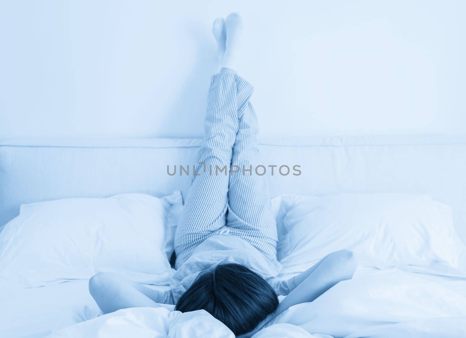 Female legs raised up high and arms under her head lying on bed in bedroom