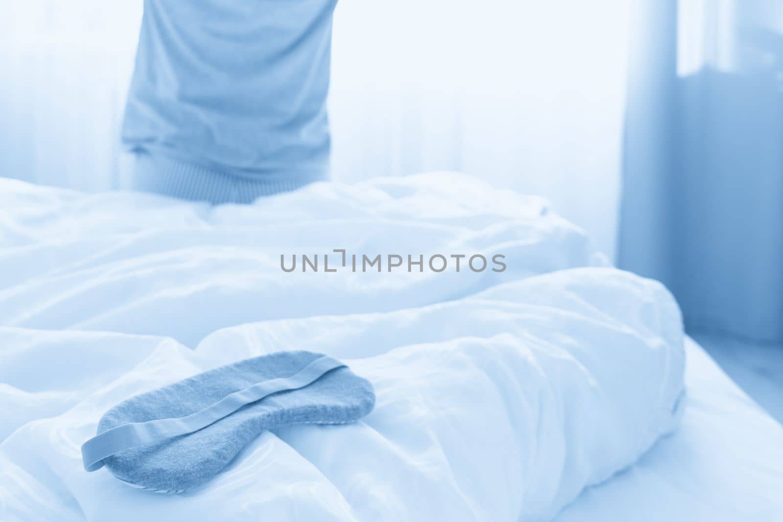 Sleeping mask on a bed with stretching woman in the background, back view