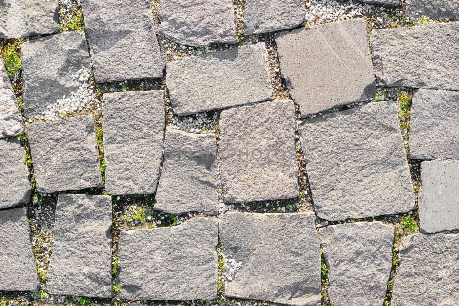 Texture of masonry roads made of asymmetrical stones with grass between masonry. by Laguna781