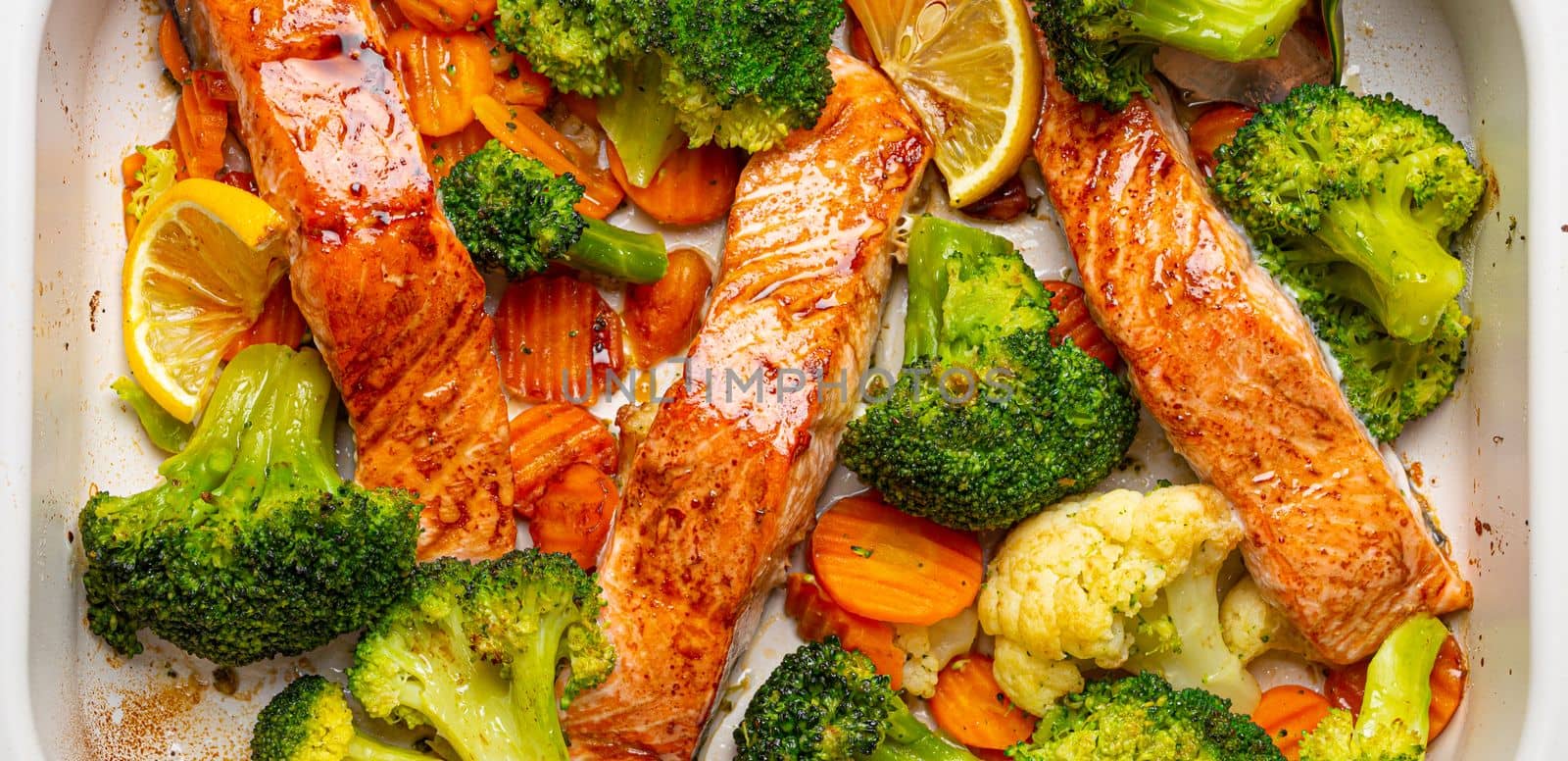 Top view close up of healthy baked fish salmon steaks, broccoli, cauliflower, carrot in casserole dish. Cooking a delicious low carb dinner, healthy nutrition concept.