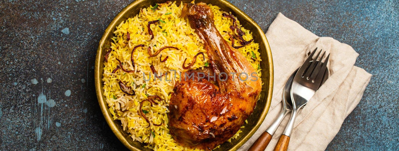 Delicious Indian dish Biryani chicken leg with basmati rice in metal brass old bowl on table rustic stone background. Traditional non-vegetarian food of India