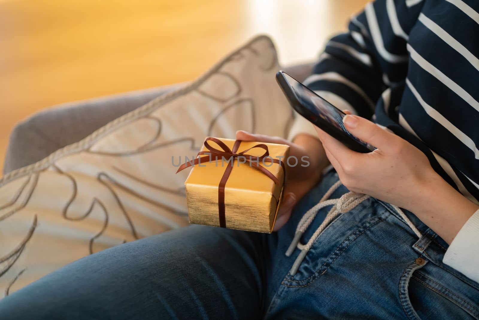 A young girl in casual clothes holds a small gift wrapped in gold paper with a red ribbon in her hands and takes a close-up photo on a mobile phone. A woman buys online a handmade, small crafts.