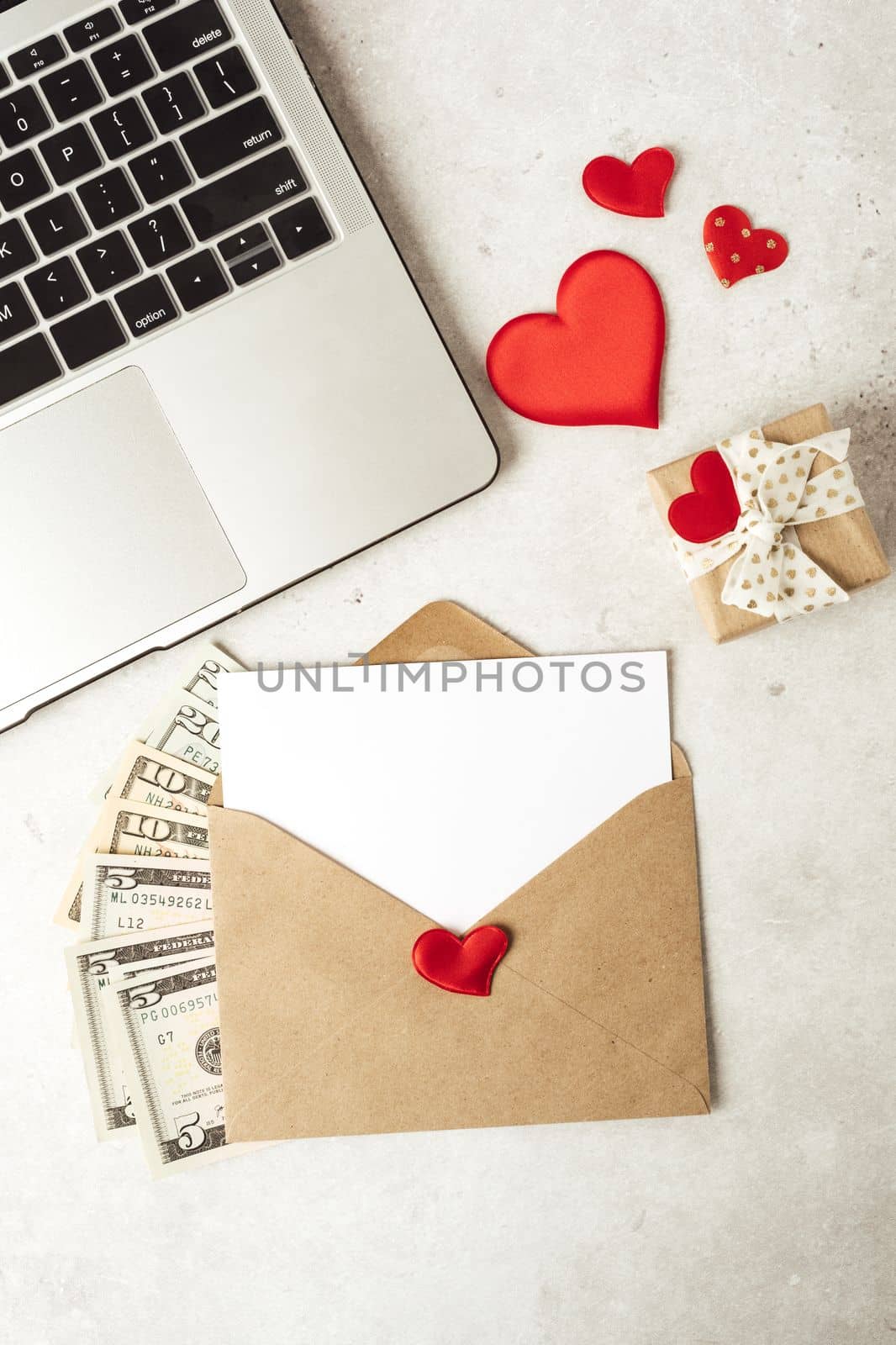 Red paper envelope with blank paper white note mockup. Flat lay of gray working table background with Valentine gift, letter, heart shape, laptop and money dollars. Top view, mock up greeting card