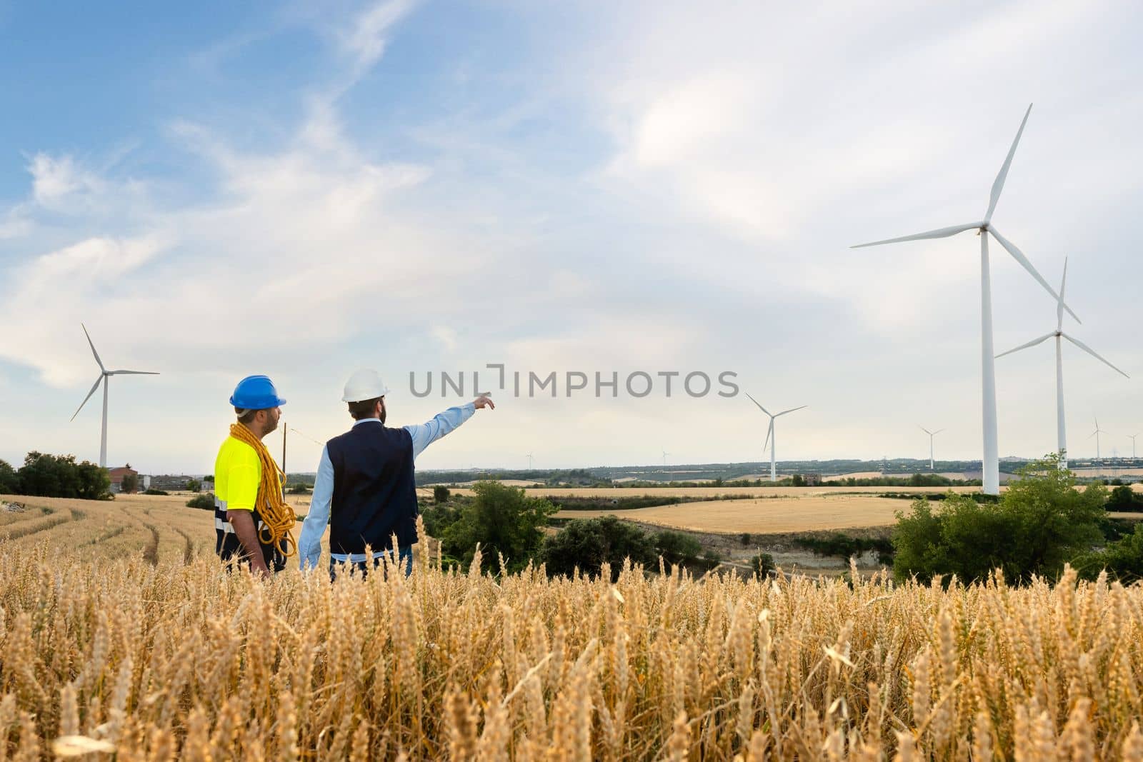 Rear view of engineer pointing at wind turbine with maintenance technician in wind farm. Copy space. by Hoverstock