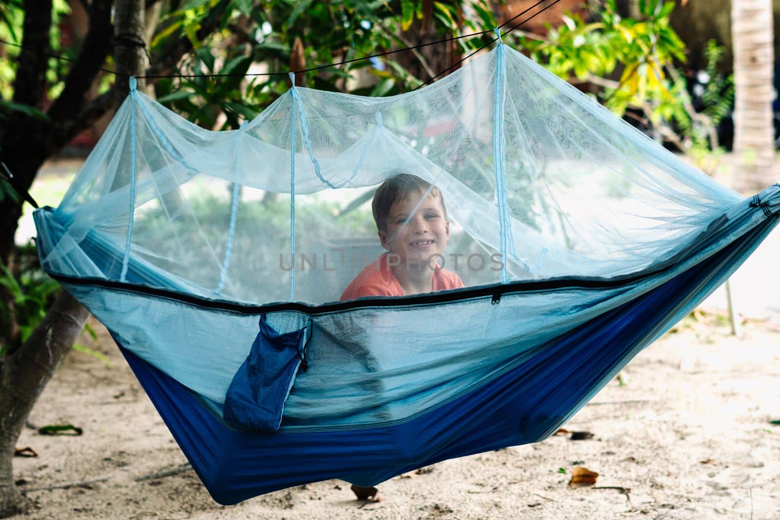 Smile child boy lie rest hammock with mosquito net. Happy childhood daydream. Look at from, laughing, portrait.