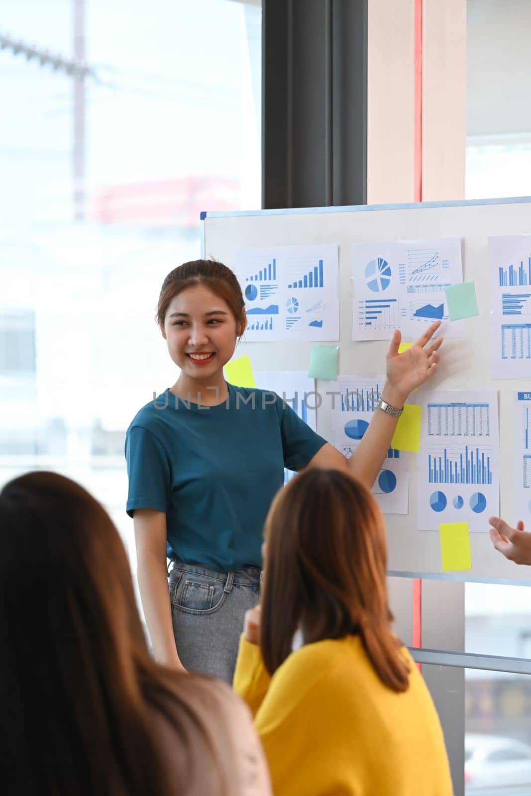 Confident young woman sharing ideas business strategy, explaining new strategies on whiteboard to her coworkers.