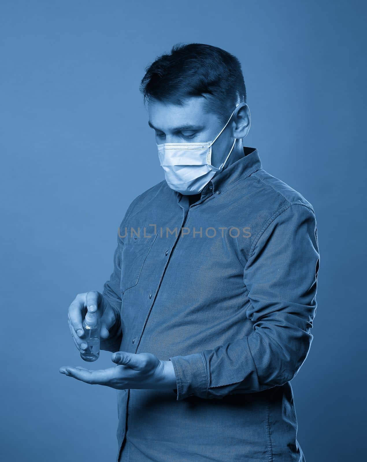 Man applying antibacterial spray on his hands on blue background by Mariakray