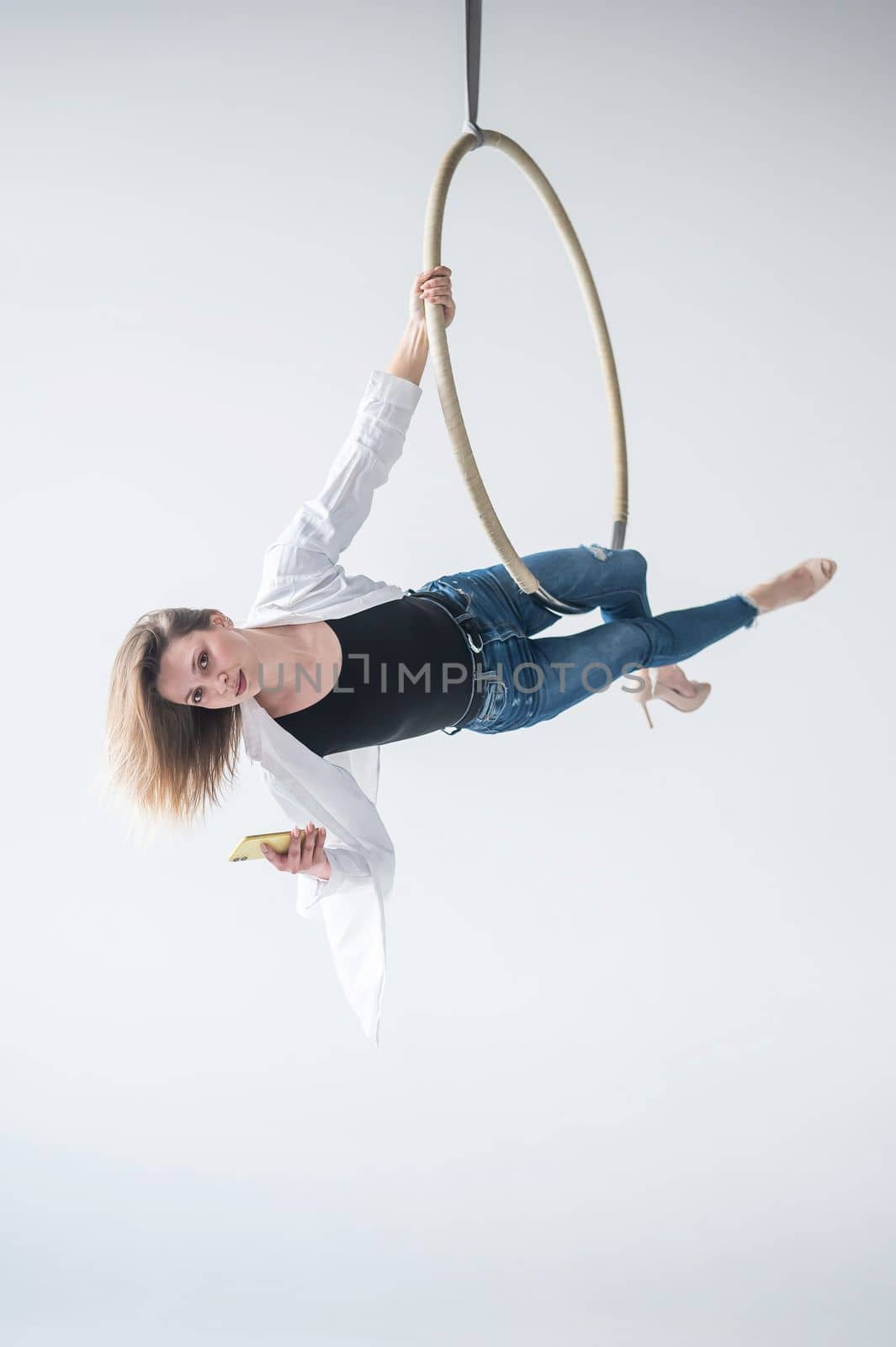 Caucasian female gymnast doing aerial hoop exercises and using smartphone