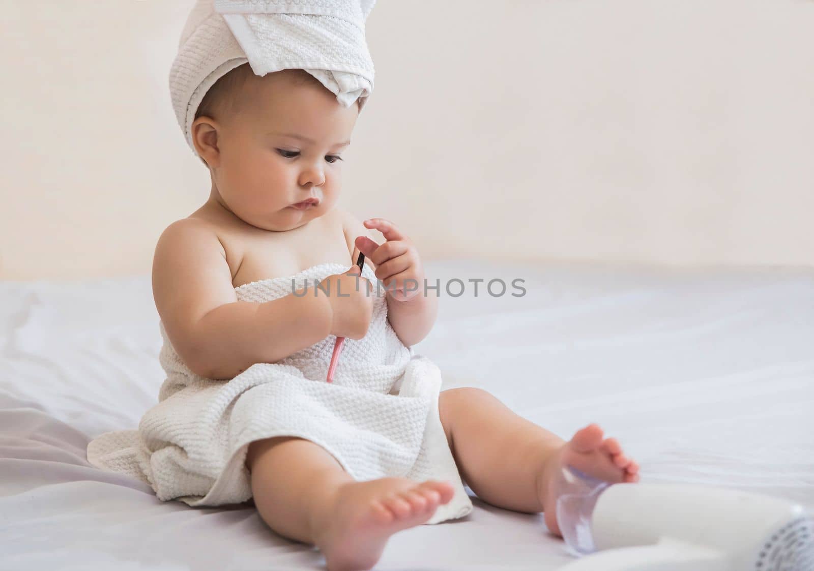 beautiful baby with a white towel on her head looks at eyeliner for eyelids on the bed