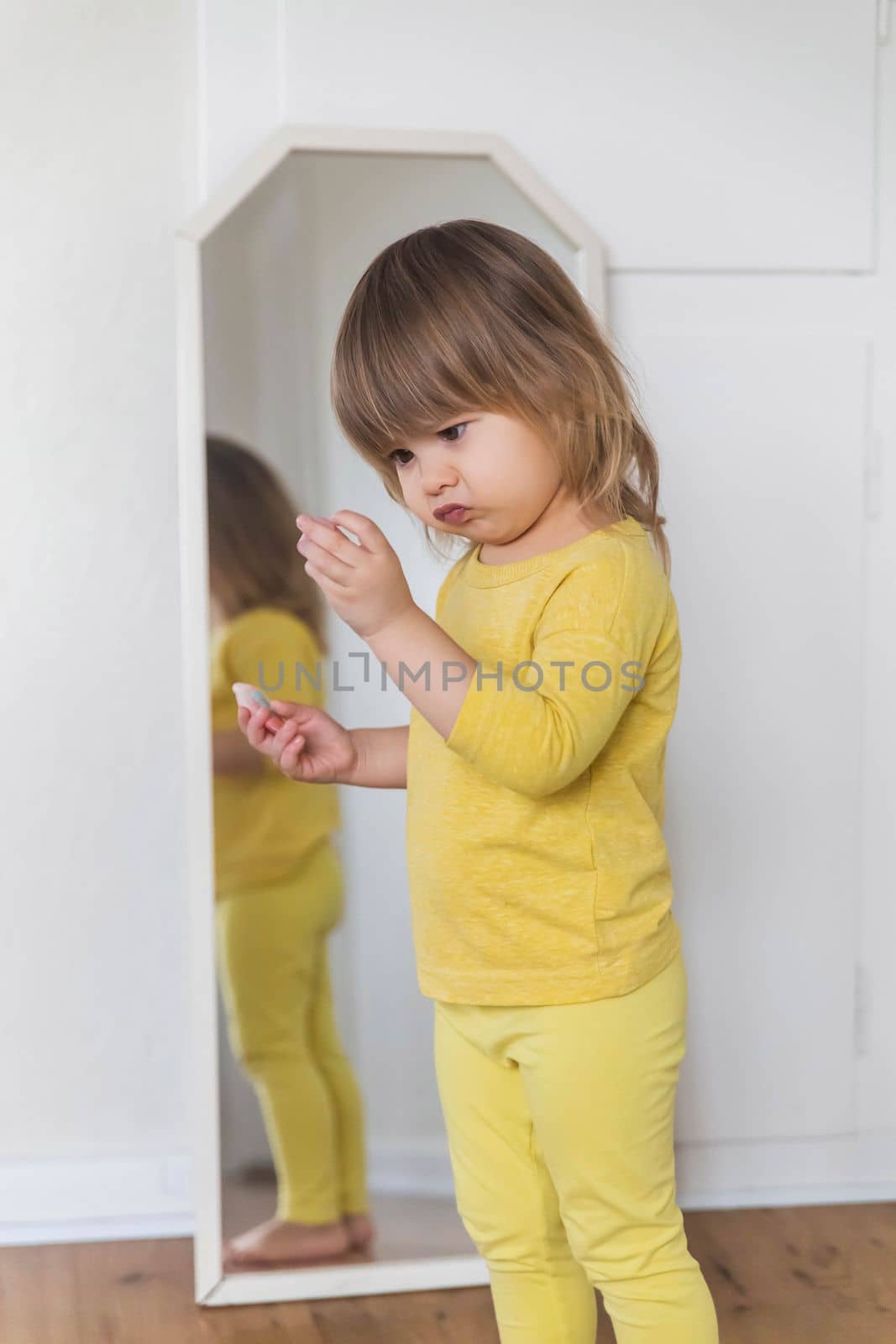 Charming baby skeptically examines some trinket near the mirror.