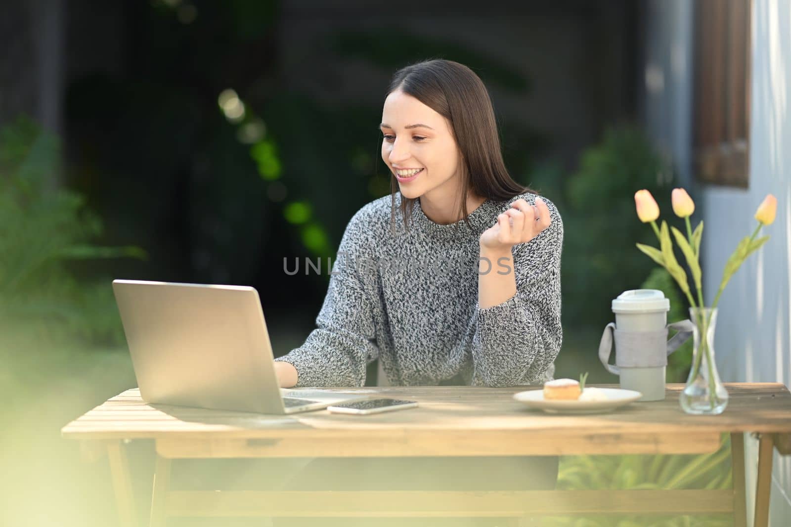 Attractive caucasian woman using laptop and working on online project remotely in outdoor cafe on sunny day.