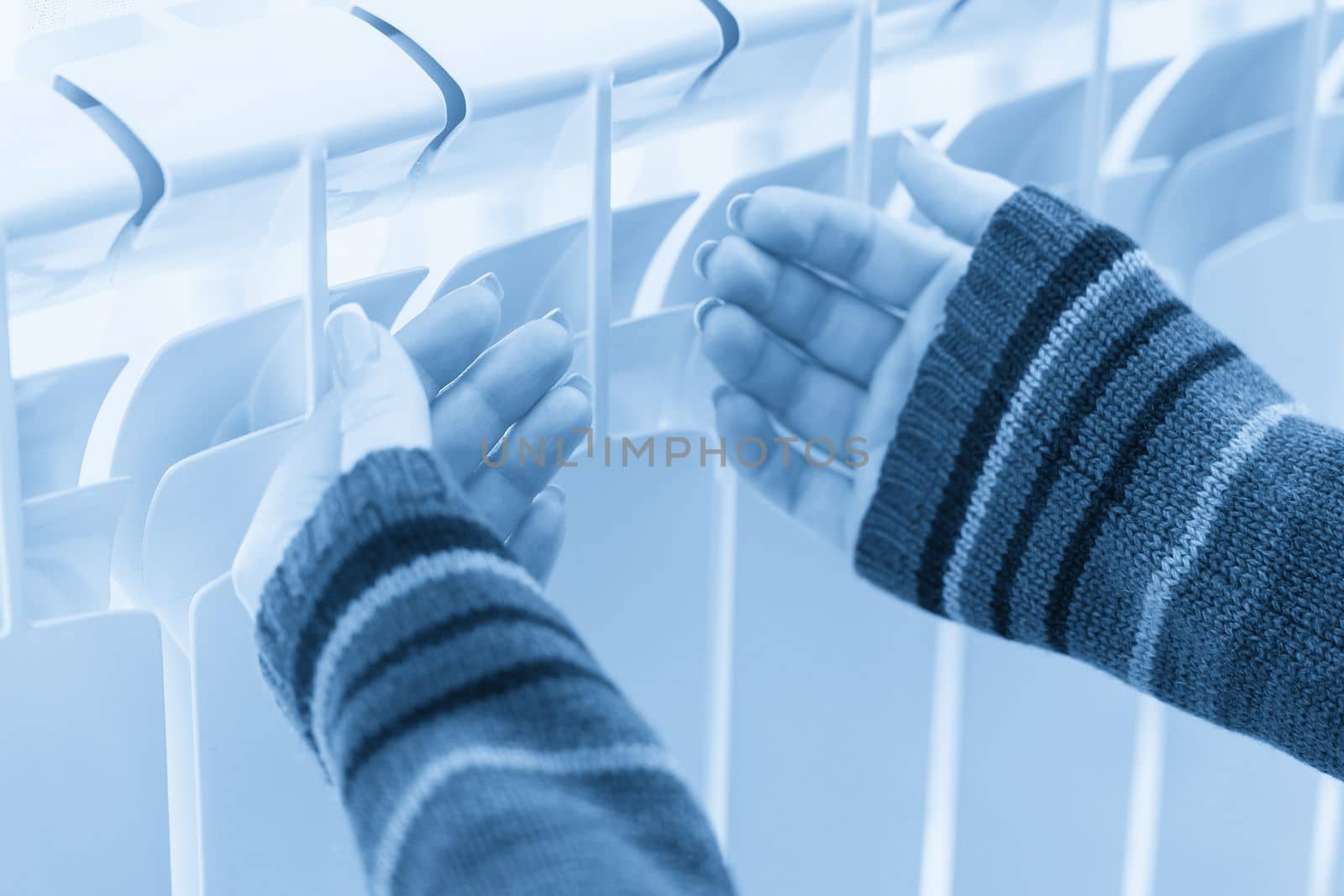 Girl warms up the frozen hands above hot radiator, close up view by Mariakray