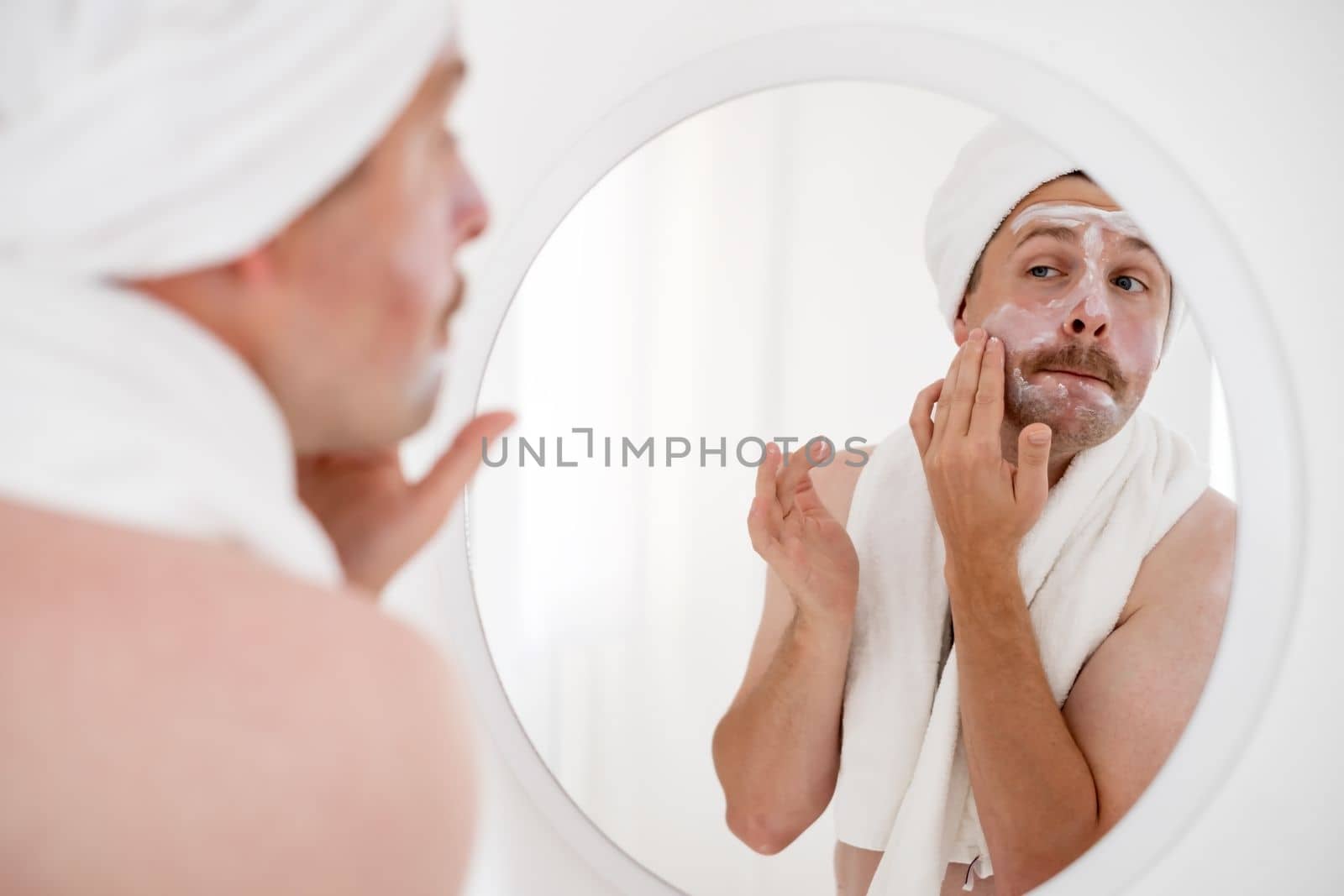 Mature man looking in mirror touch his face after shave applied aftershave cream enjoy smooth, flawless, soft skin.