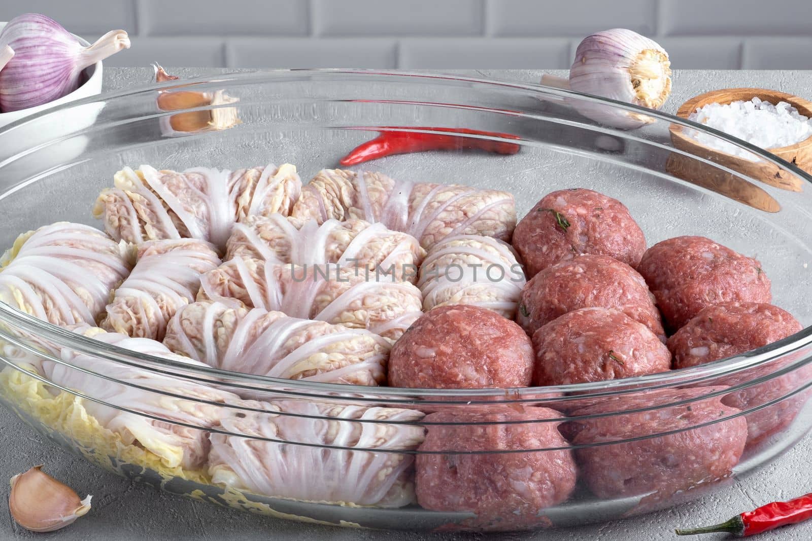 Meatballs and cabbage rolls with Chinese cabbage prepared for baking in the oven on a glass tray on the kitchen table. Healthy food. Selective focus.