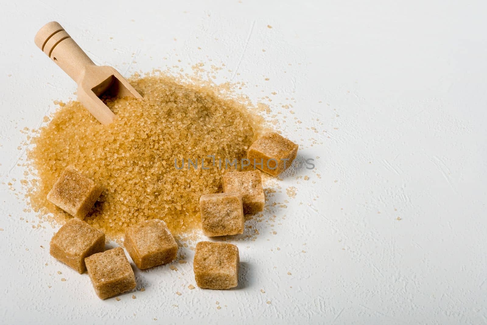 Brown cane sugar is also sprinkled in lumps on a light surface. Wooden scoop for bulk products. Selective focus. Space for text.