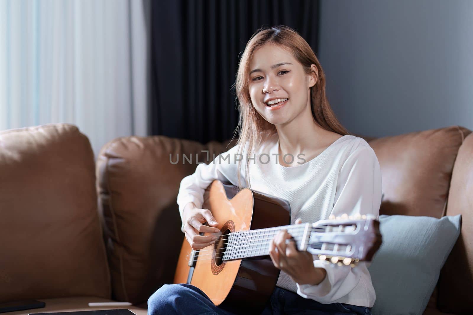 Portrait of young asian woman playing guitar on sofa relaxing stress on vacation.