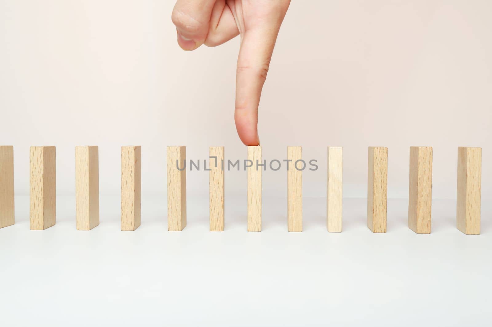 Dominoes are lined up in a row. The index finger of the hand on one wooden domino.