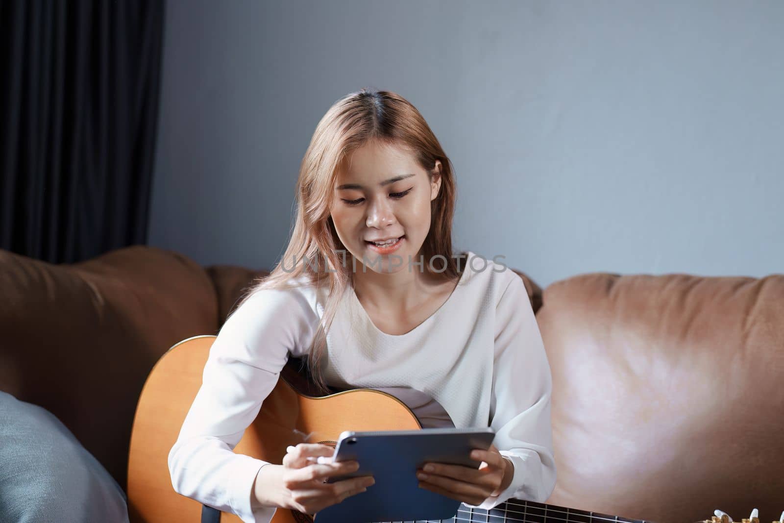 Portrait of young asian woman playing guitar on sofa relaxing stress on vacation.