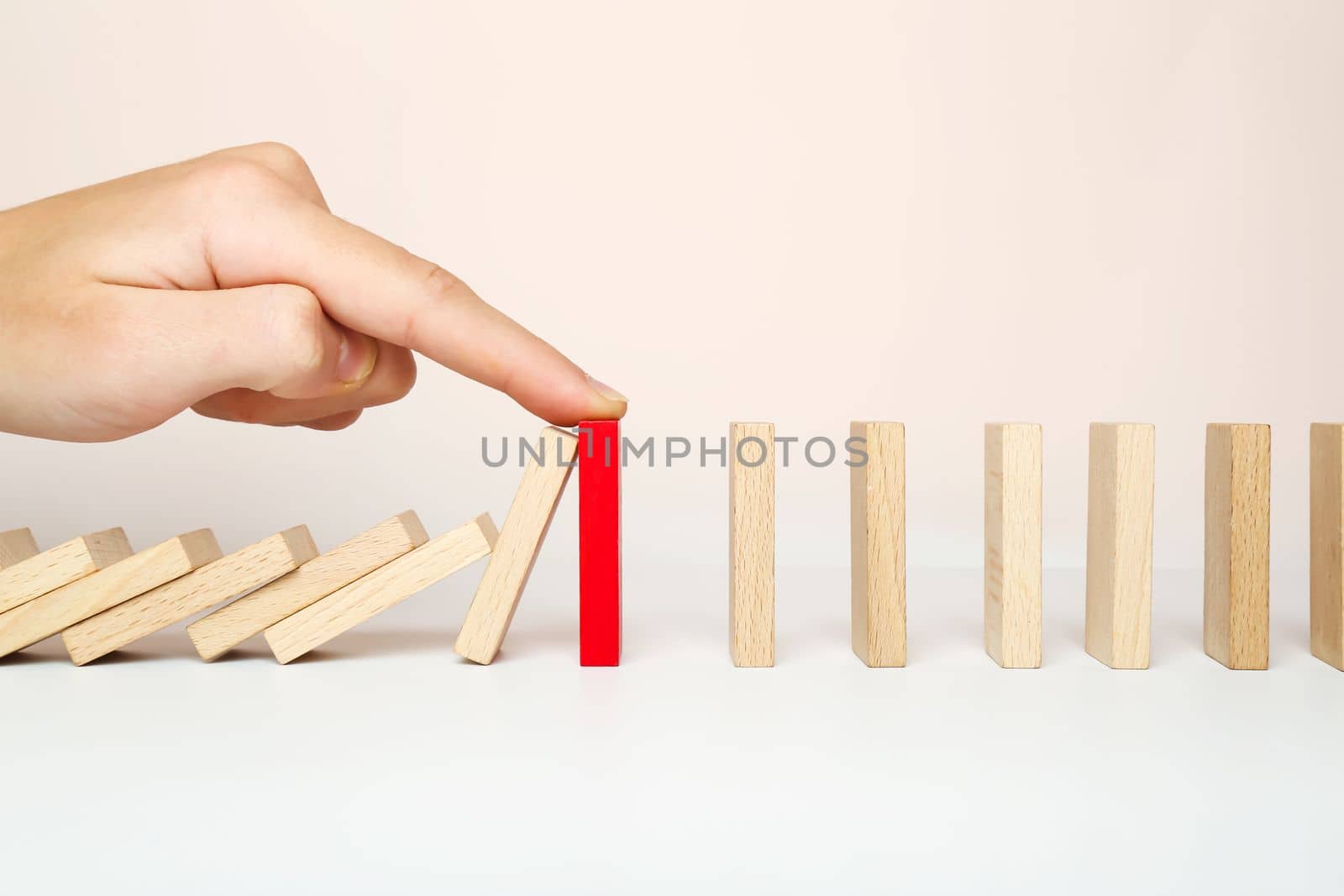 The domino falls, and the finger stops the chain reaction. The concept of solving the problem.