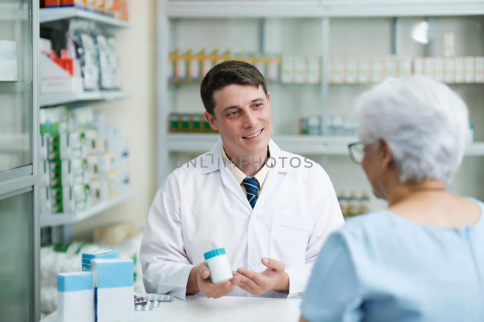 Smart male pharmacist at the drugstore wearing white gown talking, giving advice, explaining, suggesting, and recommending to client or patient about the prescription and medications. Medicine and healthcare concept.
