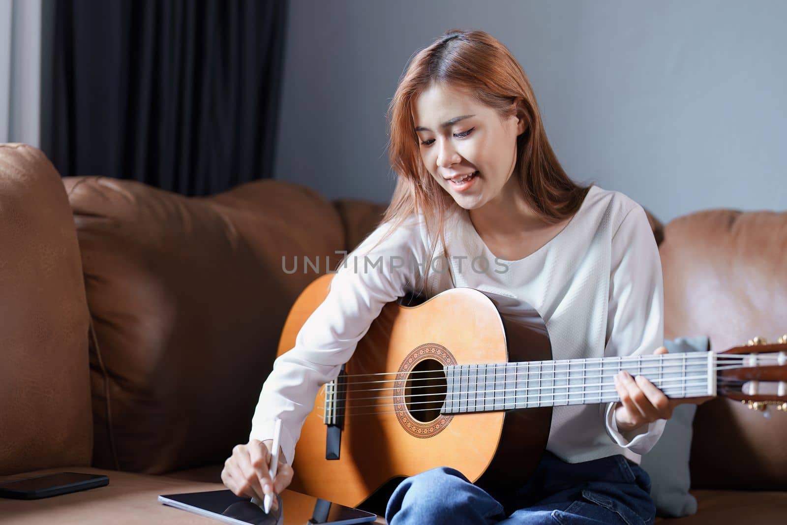 Portrait of young asian woman playing guitar on sofa relaxing stress on vacation.