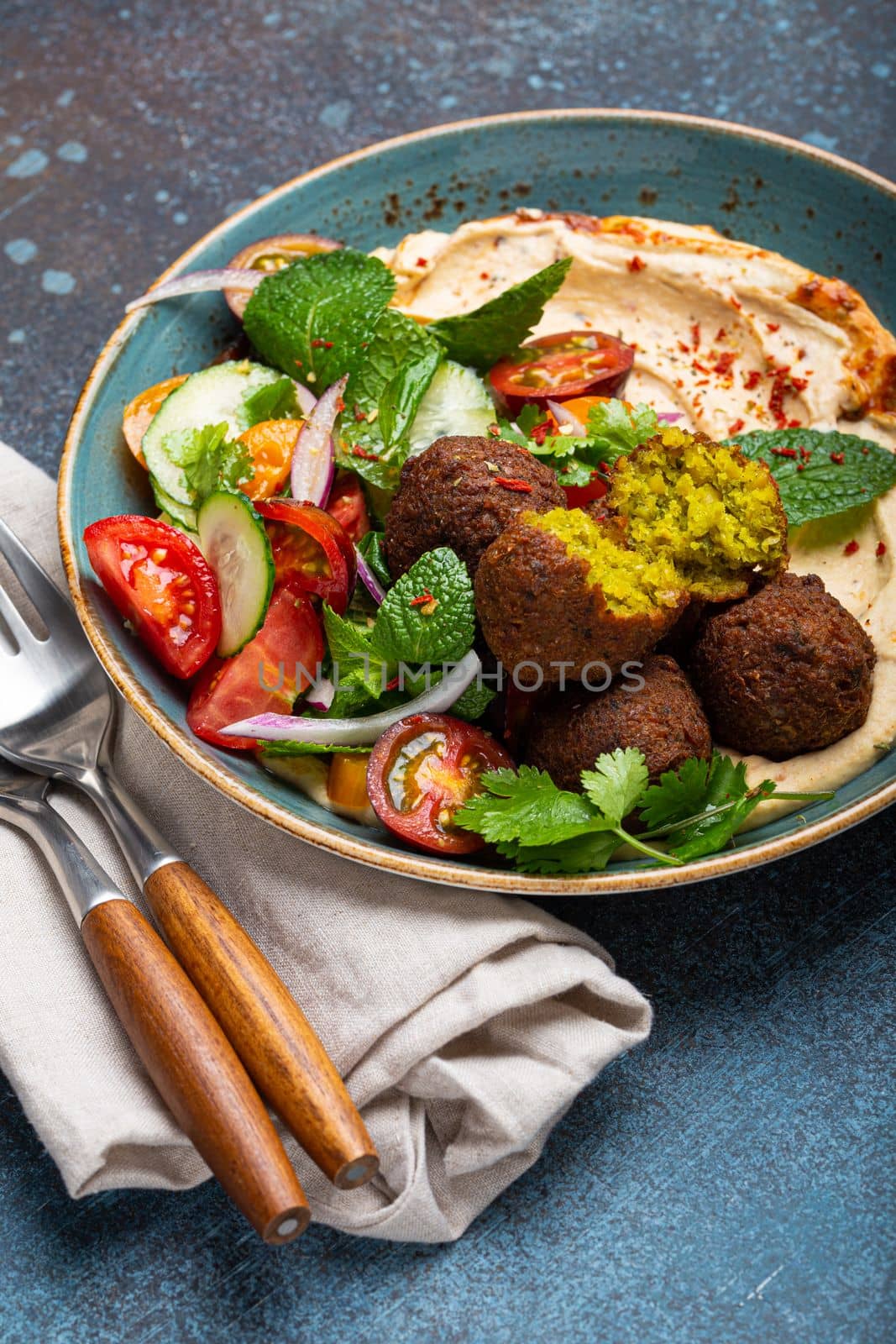 Close up of Middle Eastern Arab meal with fried falafel, hummus, vegetables salad with fresh green cilantro and mint leaves on ceramic plate on stone rustic background table. Arabic traditional cuisine