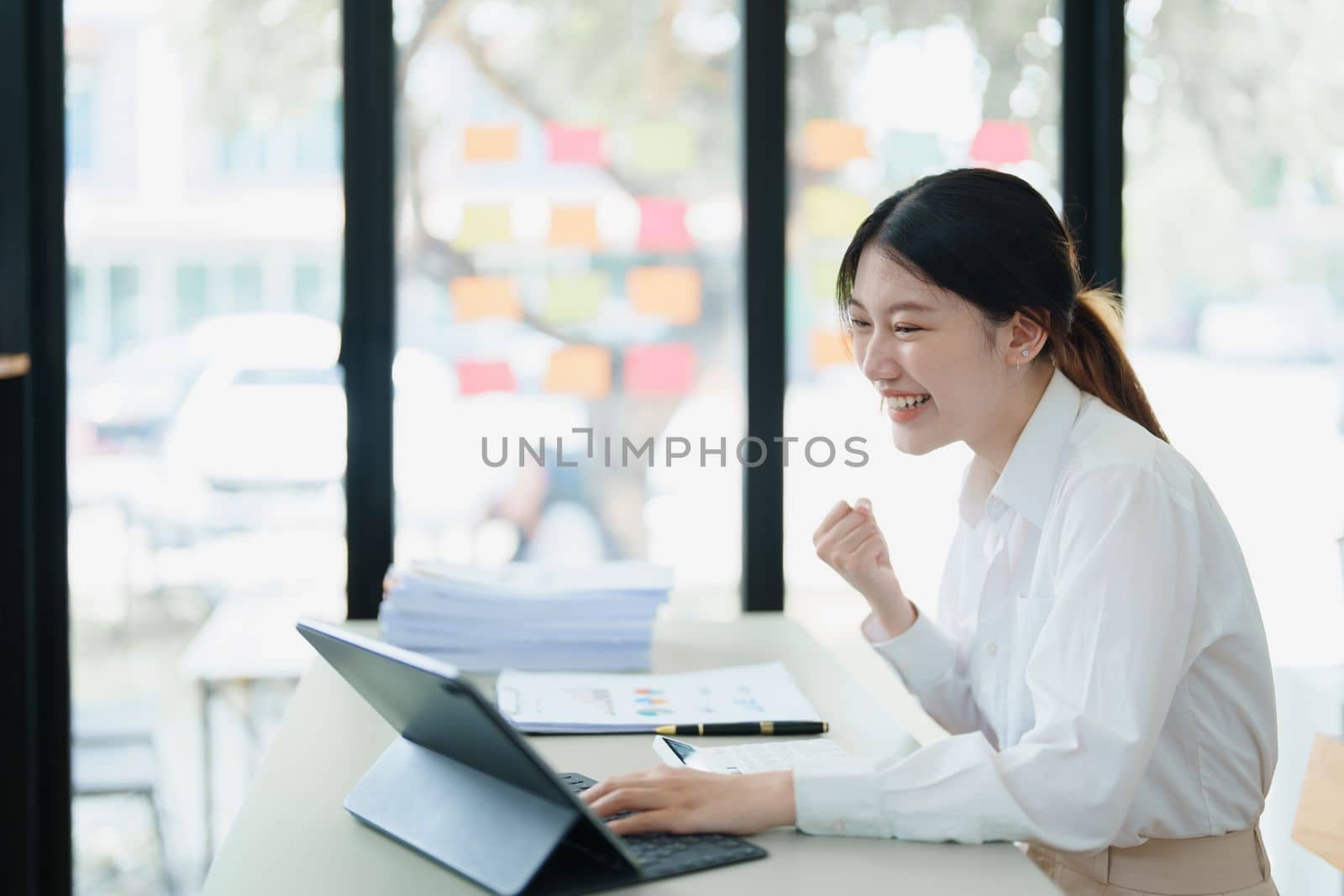 Portrait of a woman business owner showing a happy smiling face as he has successfully invested her business using computers and financial budget documents at work.