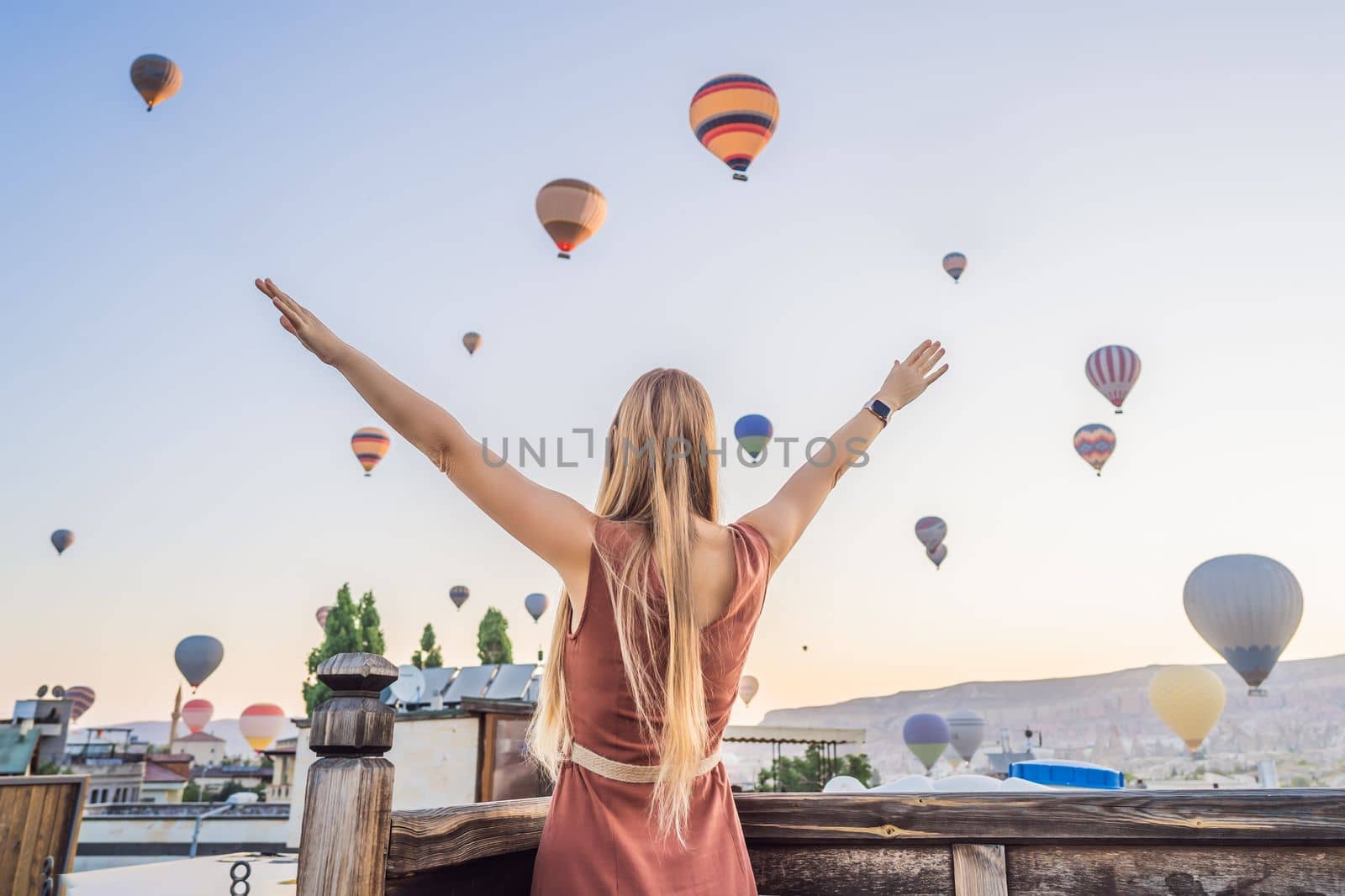Tourist woman looking at hot air balloons in Cappadocia, Turkey. Happy Travel in Turkey concept. Woman on a mountain top enjoying wonderful view.