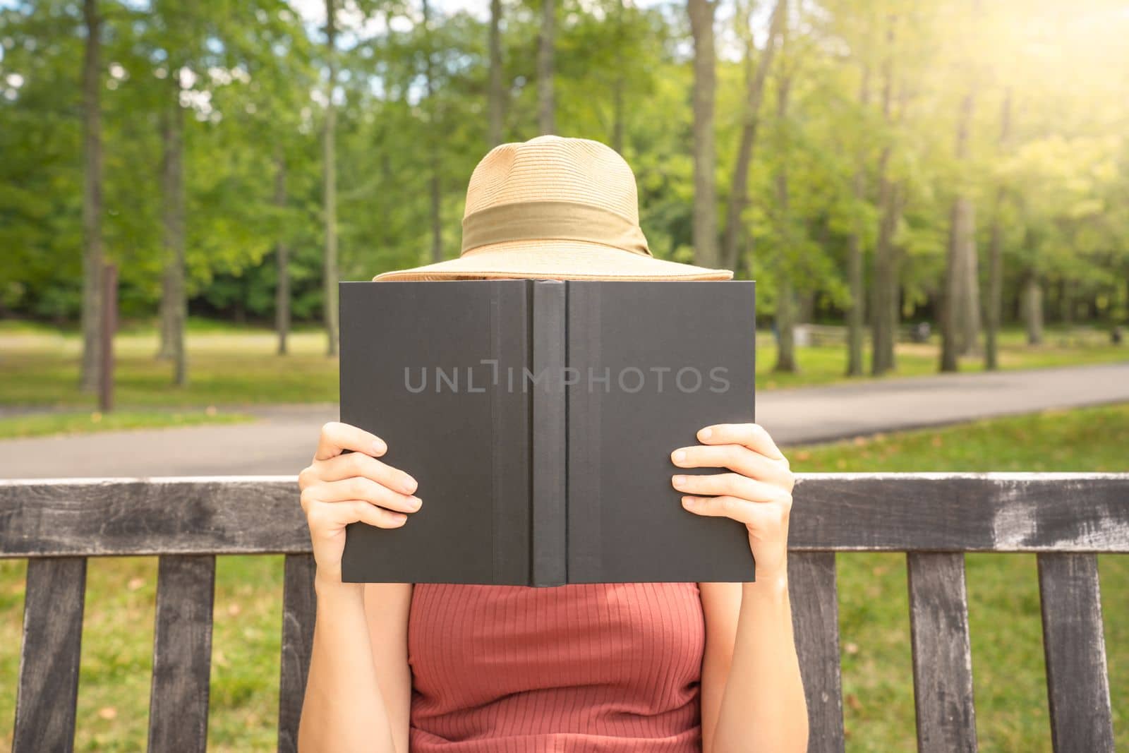 Unrecognizable young woman sitting on park bench and reading a book. High quality photo