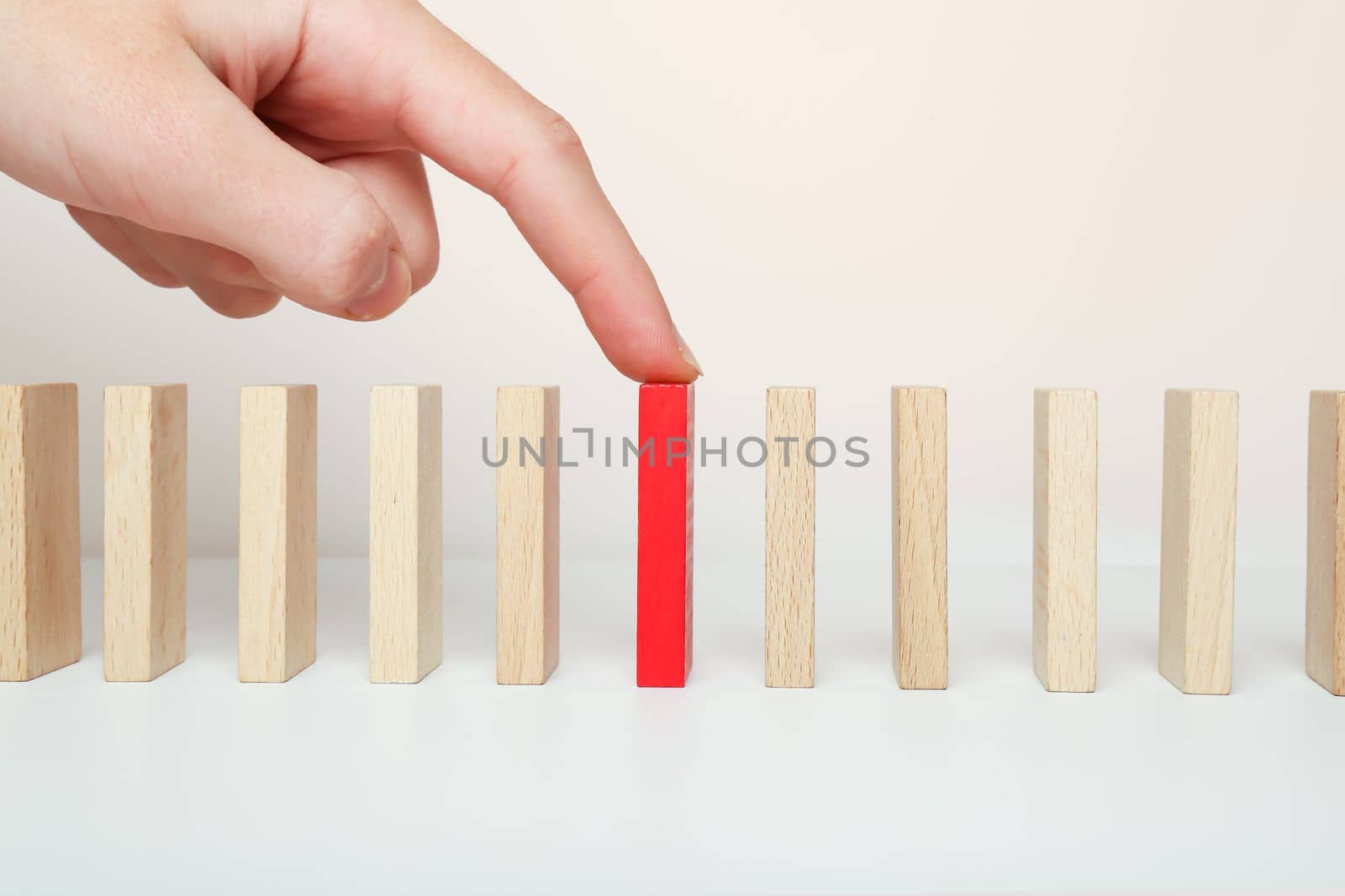 Domino stands and his finger points to the red one among all the wooden ones. Index finger on the domino