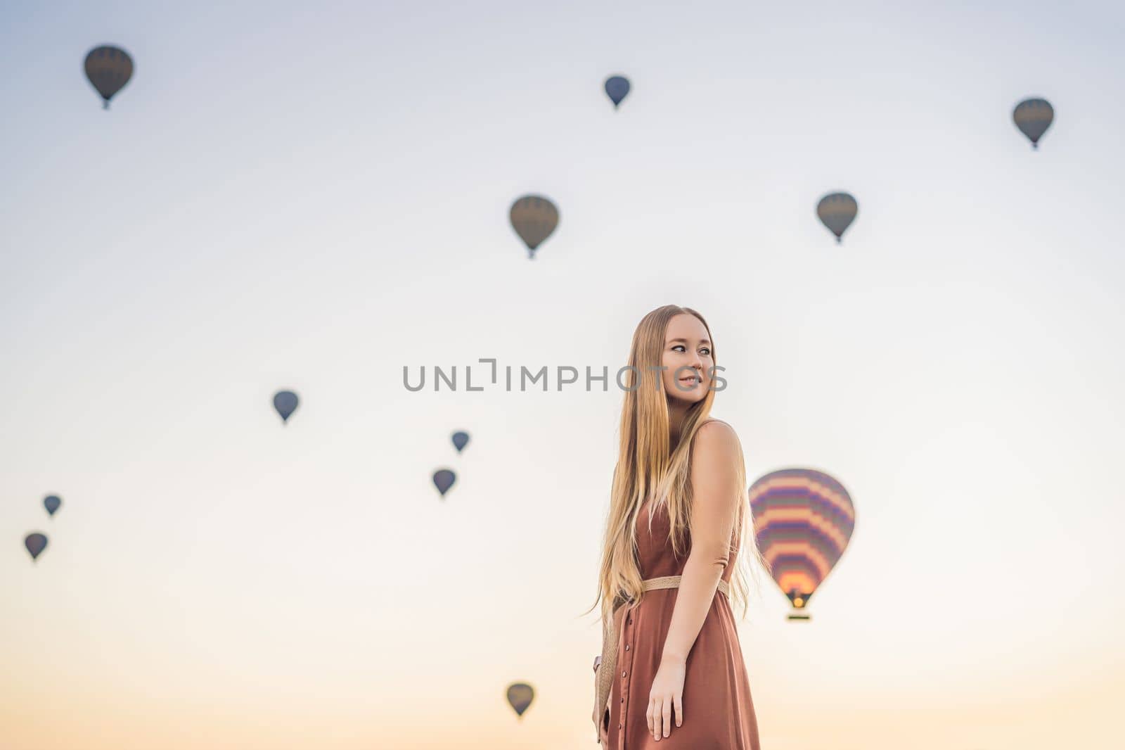 Tourist woman looking at hot air balloons in Cappadocia, Turkey. Happy Travel in Turkey concept. Woman on a mountain top enjoying wonderful view.