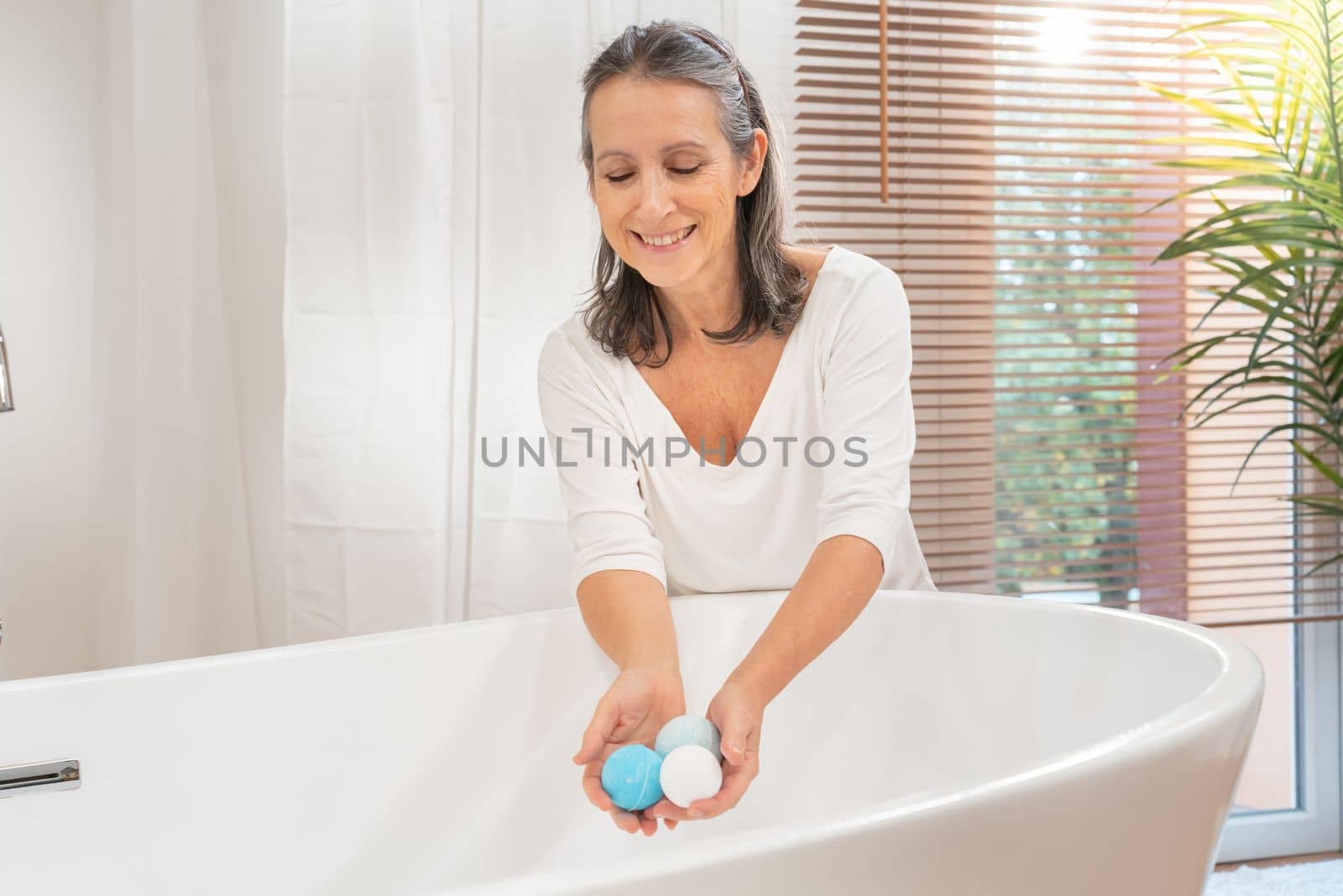 Happy smiling beautiful middle aged woman with salt soap aroma balls at luxury bathtub. Bodycare spa procedures antiage recreation skin care, cosmetic and beauty concept.
