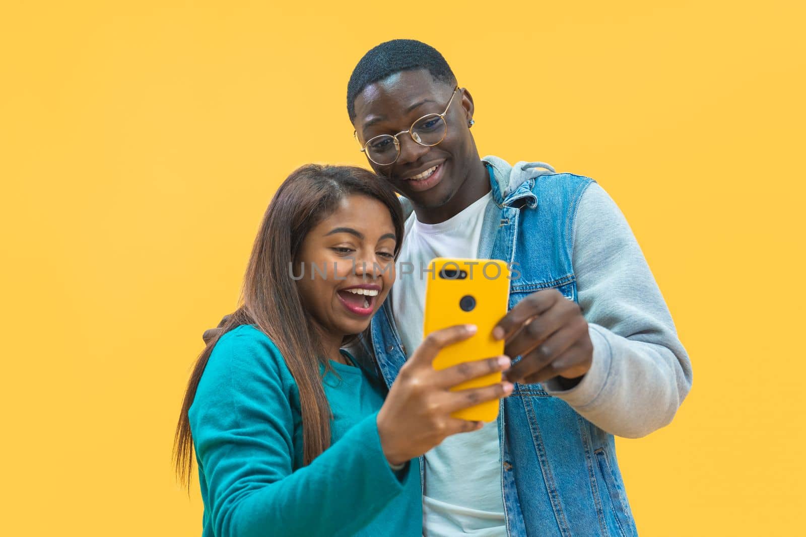 Excited African American couple looking at smart phone screen together isolated on yellow background. Joyful black man and woman using cellphone together, entertainment concept. High quality photo