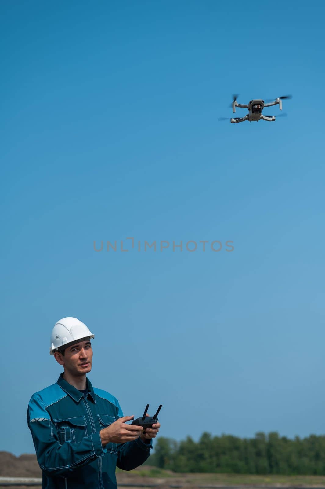 A man in a helmet and overalls controls a drone at a construction site. The builder carries out technical oversight. by mrwed54