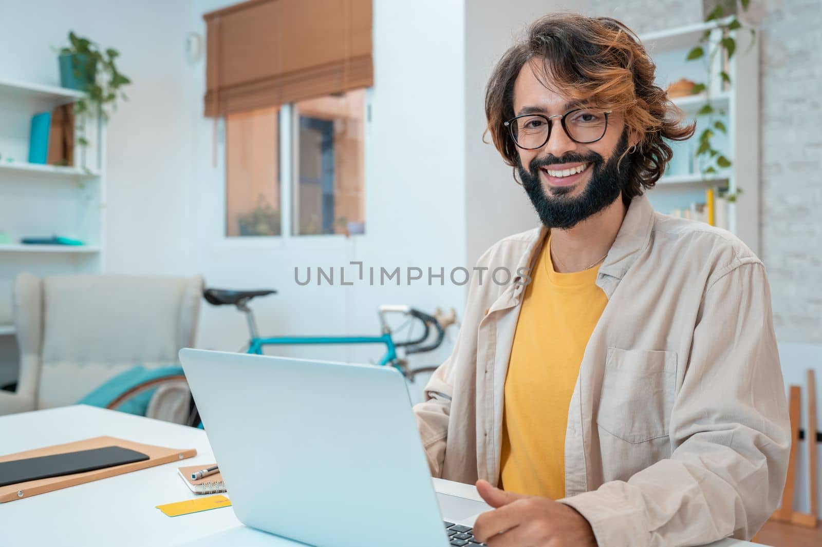 Successful hispanic male freelancer at the workplace, looks directly at the camera, smiling. Joyful handsome guy at webinar training or online conference. High quality photo