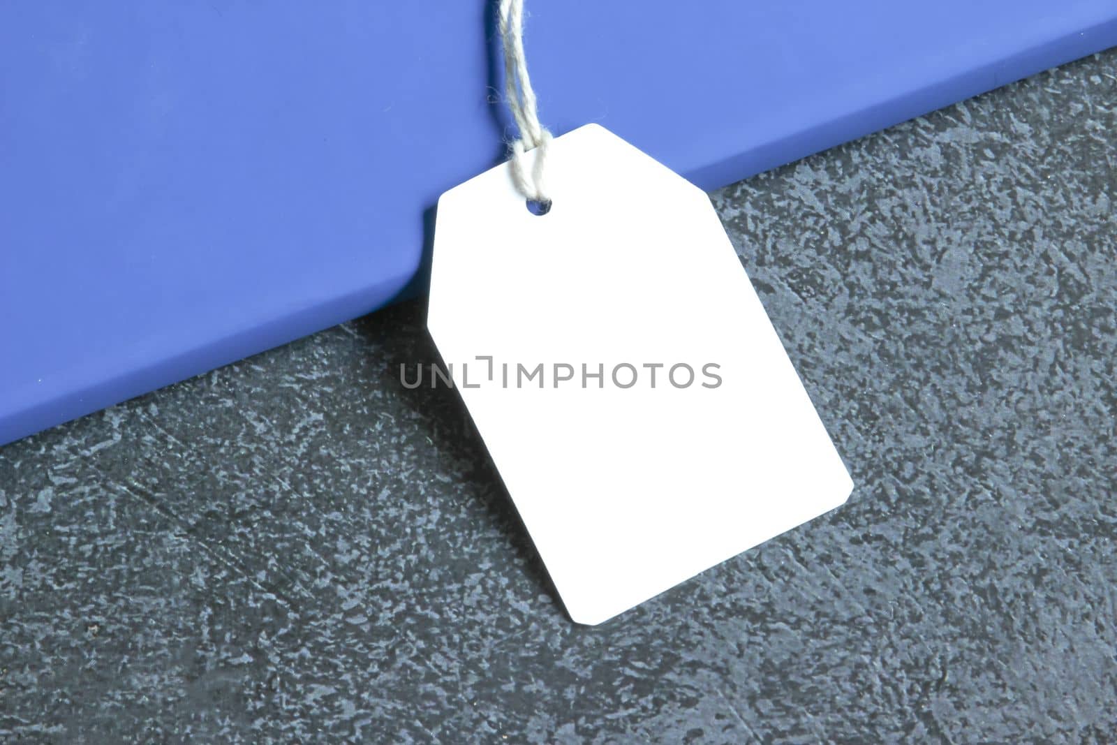 Rectangle white gift tag mockup with white cord, close up on blue book and black background. Blank paper rectangular price tag mockup, Sale and Black Friday concept, element for design, label mockup