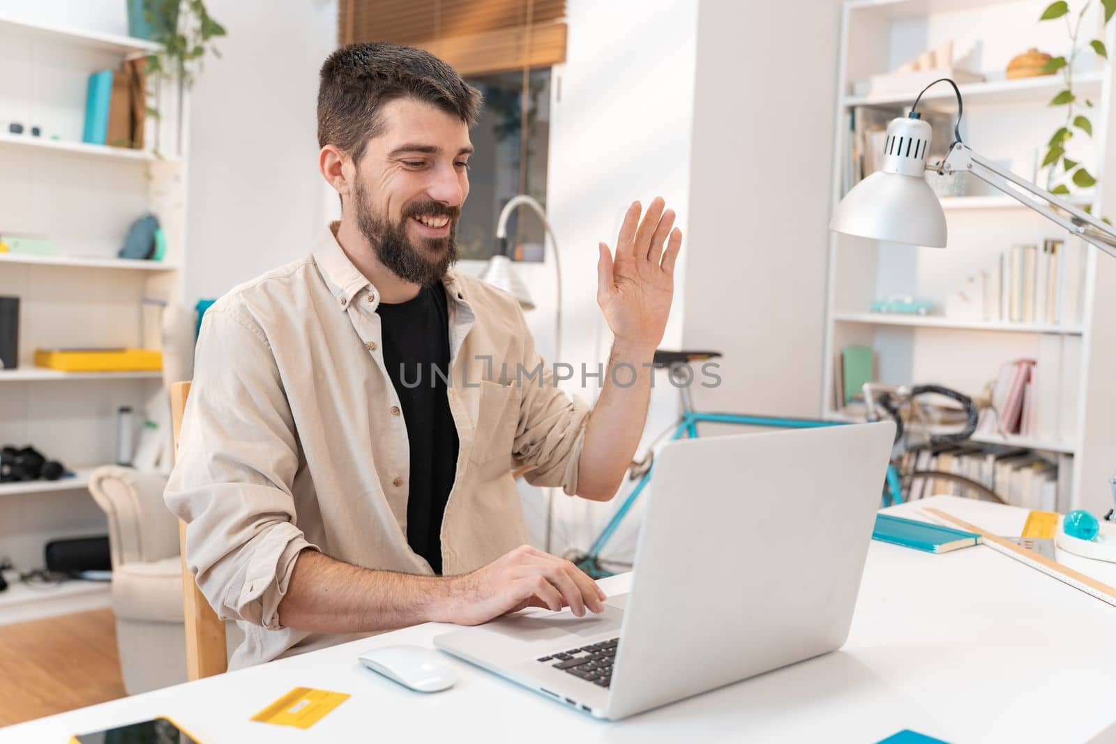 Happy male making a video call from home with his laptop. Young man smiling saying hello to their family, friends or work colleagues on computer desk. Working remotely concept. High quality photo