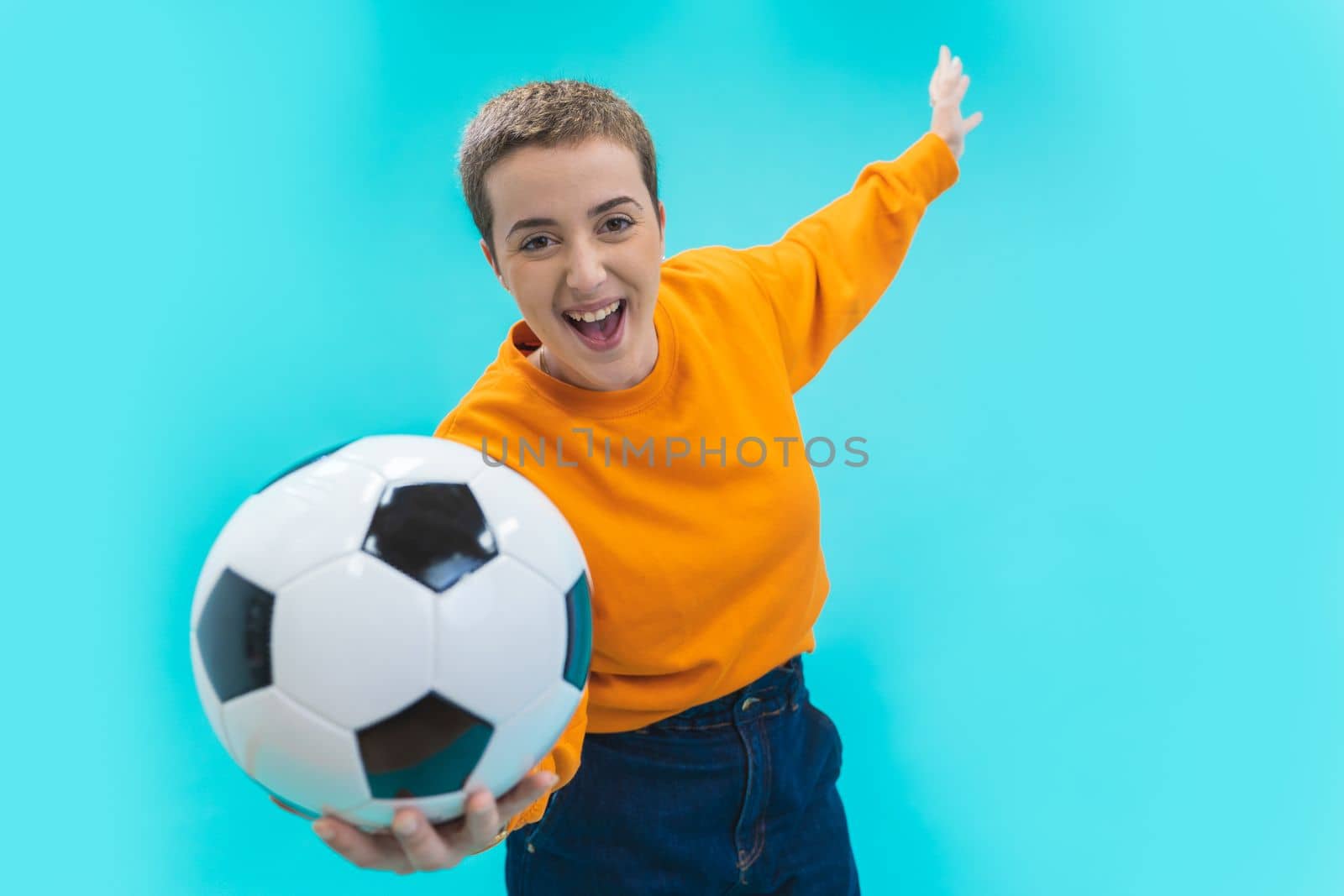 Screaming young woman girl football soccer fan in orange sweater isolated on blue background. by PaulCarr