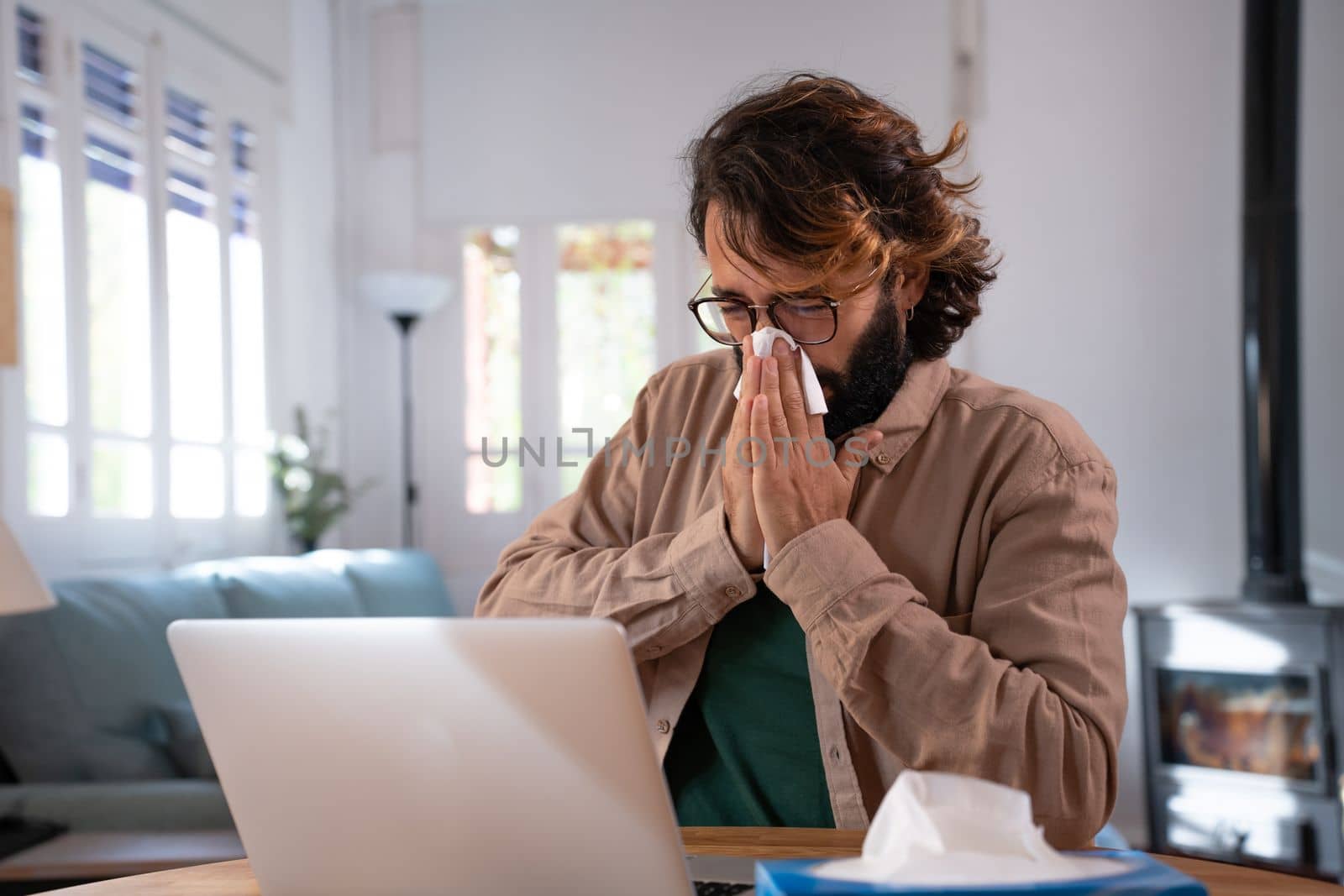 Sick young man snotting and working at home with laptop . High quality photo