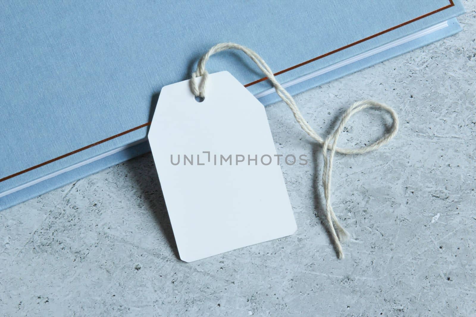 Rectangle white gift tag mockup with white card, close up on blue book and grey background. Blank paper rectangular price tag mockup, Sale and Black Friday concept, element for design, label mockup
